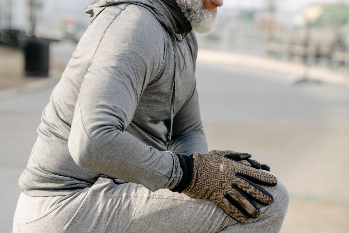 Older man stretching his legs outdoors in a city park before exercising