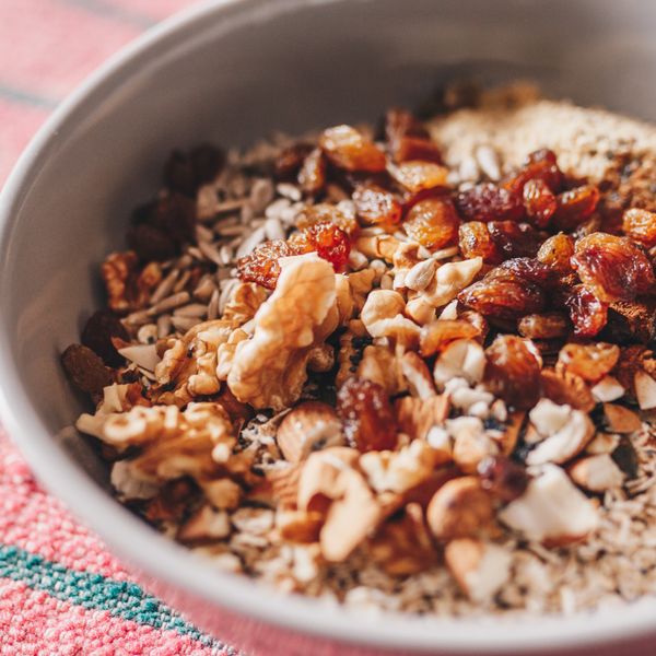 White bowl of oats topped with walnuts, sunflower seeds and raisins