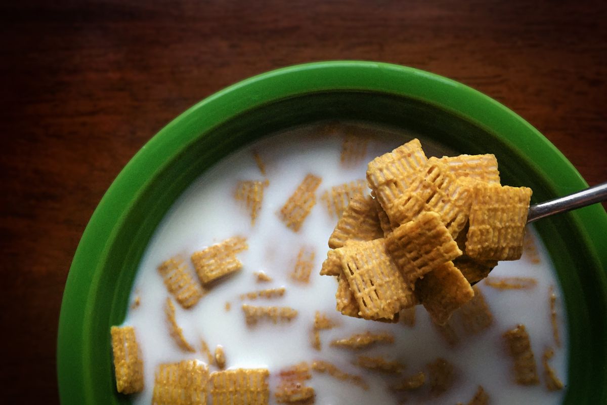 Top-down view of a green bowl of cereal in milk with a spoonful lifted out